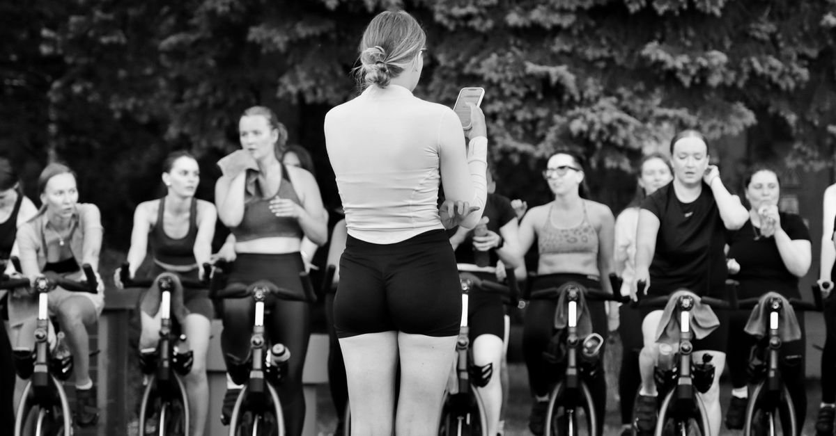 Grupo em aula de spinning ao ar livre com instrutora à frente