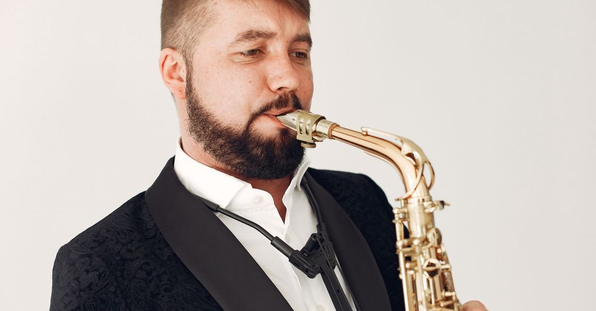 Músico de terno preto tocando saxofone em fundo claro