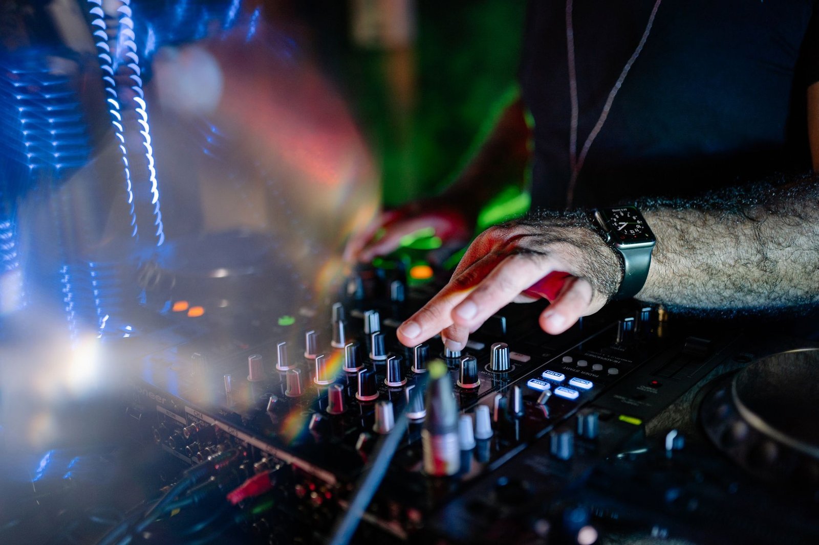 Mãos de um DJ ajustando os botões de uma mesa de som em ambiente escuro