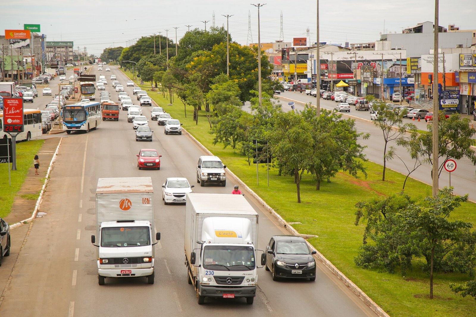 Avenida movimentada de Taguatinga com onibus, caminhoes e o comercio da via lateral