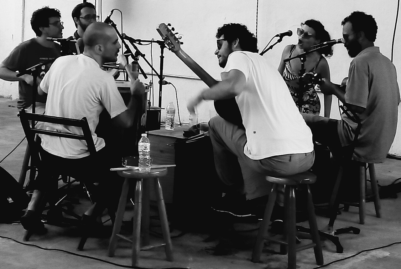 Músicos tocam em roda de samba sentados em torno de uma mesa, imagem ilustrativa