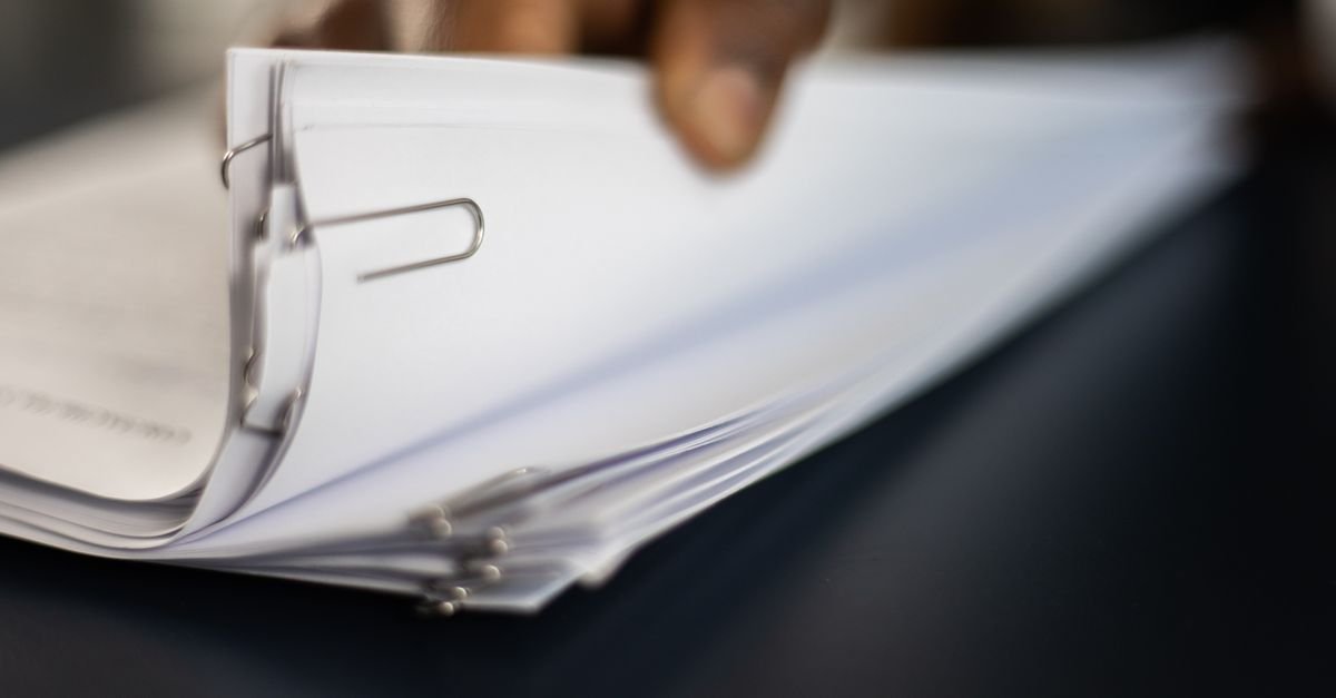 Pilha de folhas de papel presas por clipes metálicos sobre mesa escura, em close
