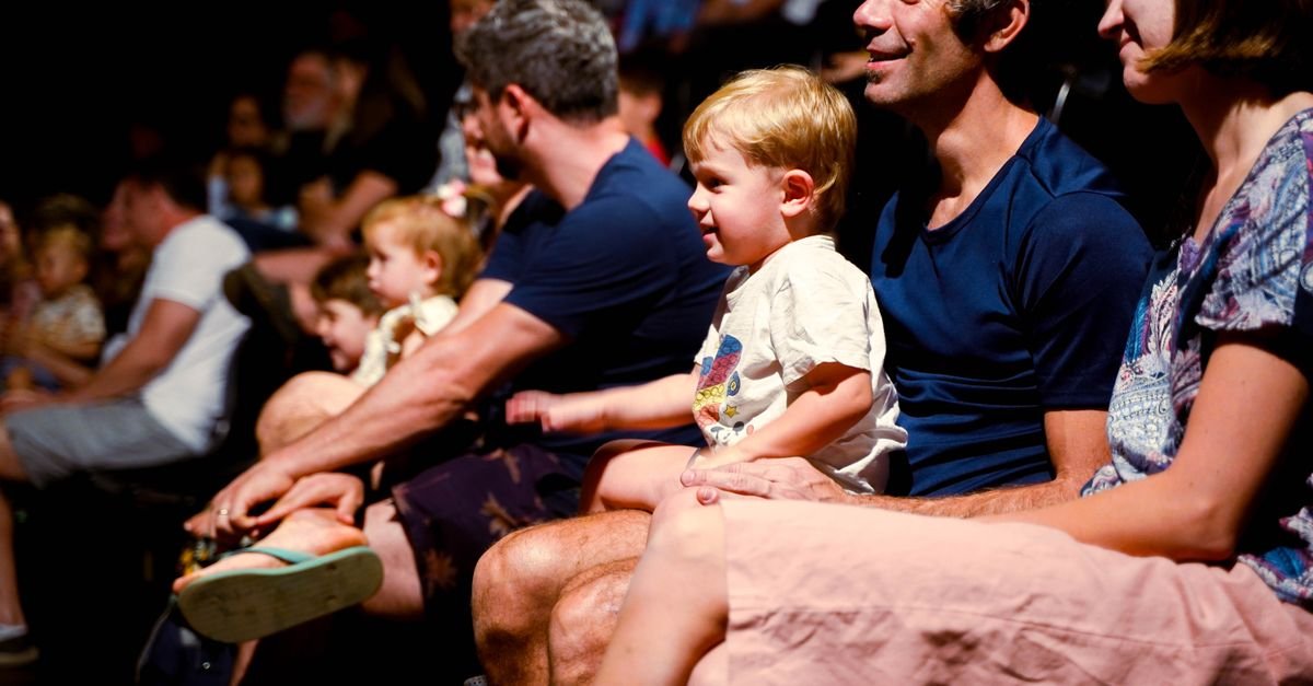 Plateia com famílias e crianças assistindo a uma apresentação em teatro