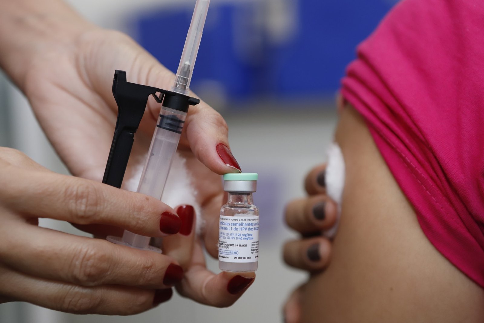 Profissional de saúde segura frasco de vacina contra o HPV e seringa durante aplicação em braço de paciente