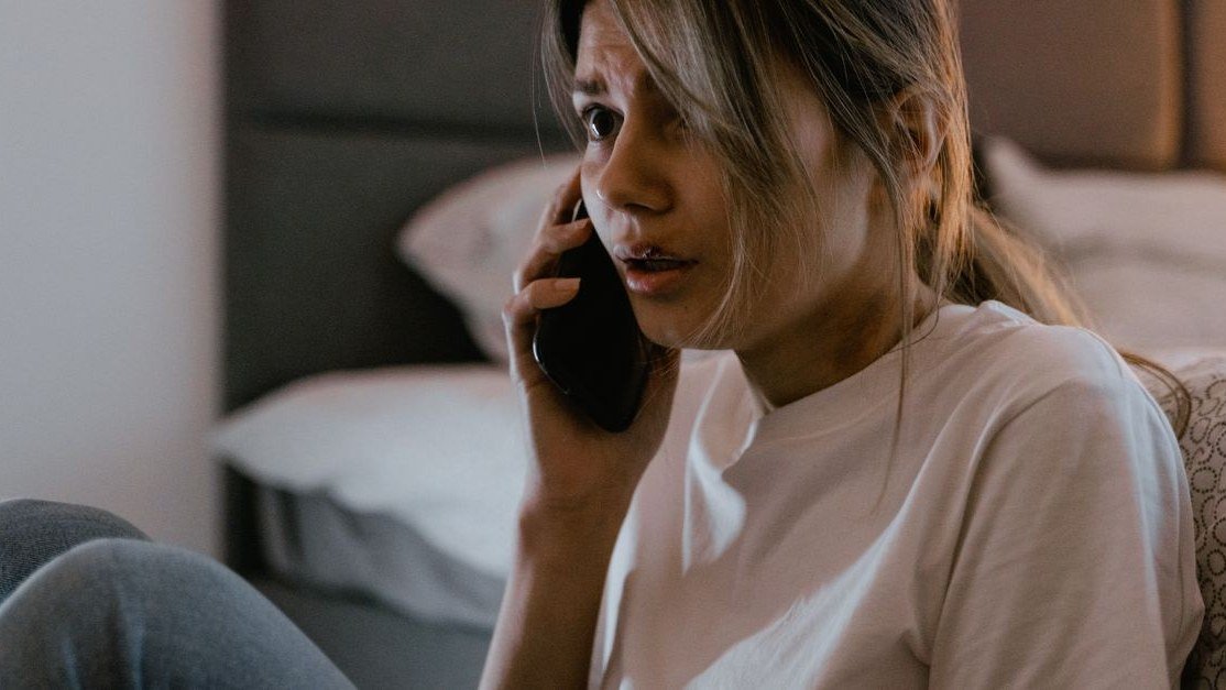 Mulher com expressão preocupada falando ao celular dentro de casa
