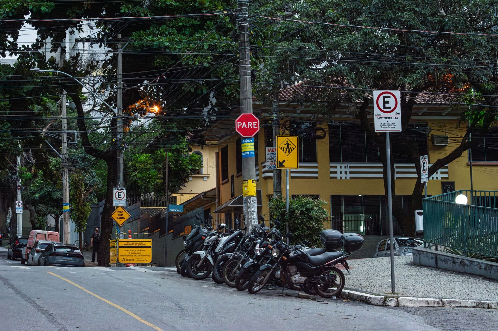Motocicletas estacionadas em vaga sinalizada na rua, ao lado de placa de parada obrigatória