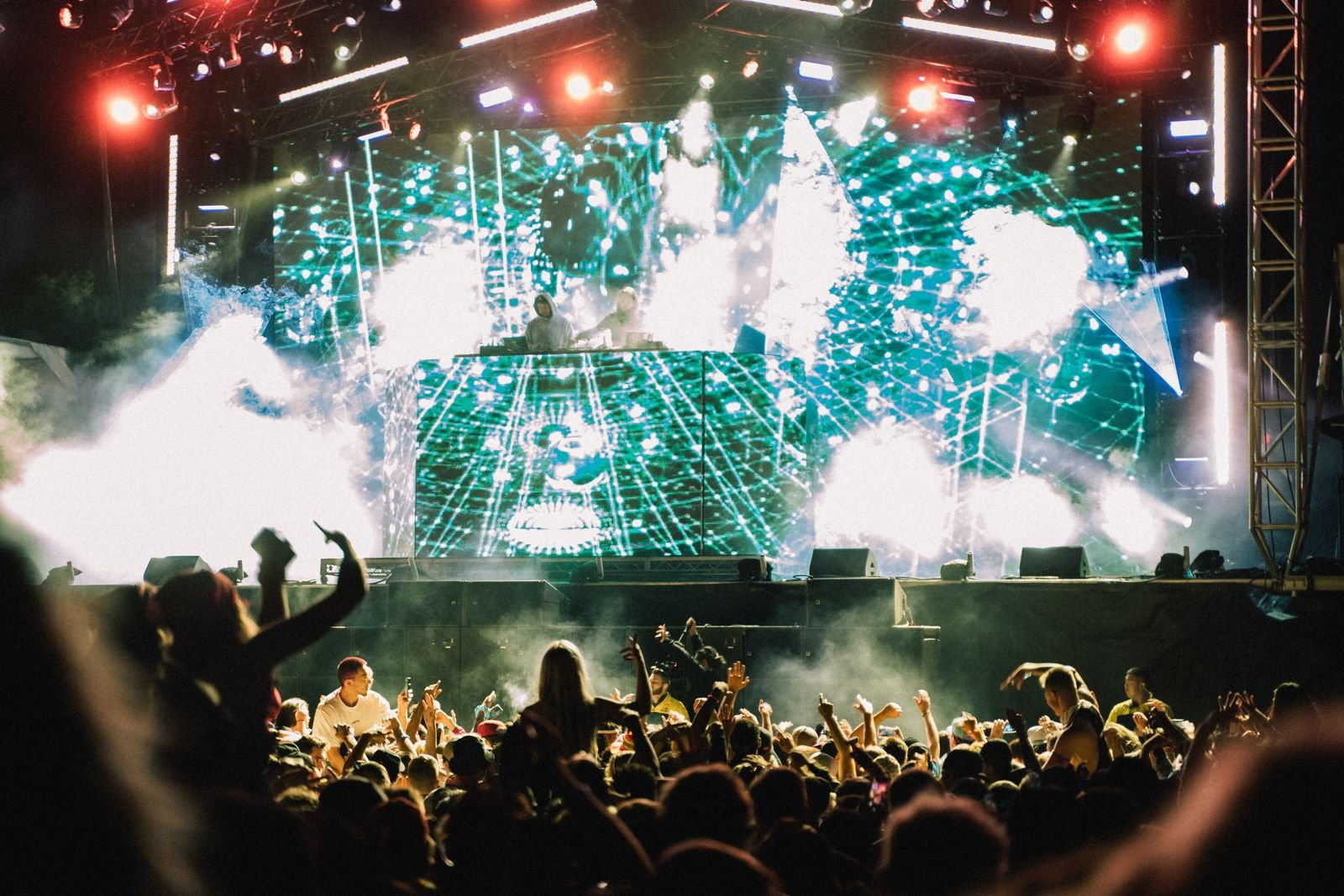 DJs em palco com telão de projeções e público de braços erguidos