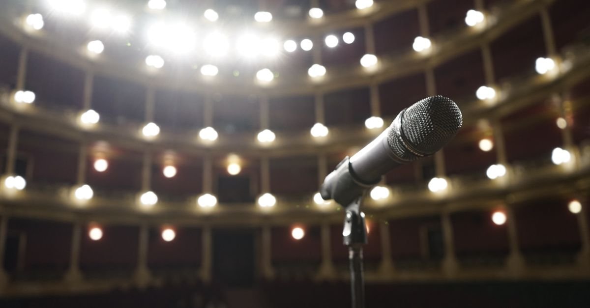 Microfone em pedestal no palco de um teatro com luzes acesas ao fundo