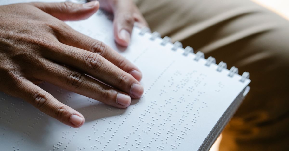 Mãos passando os dedos sobre página com texto em braille