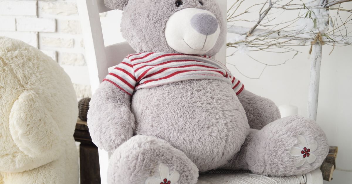 Urso de pelúcia cinza com camiseta listrada sentado sozinho em uma cadeira branca