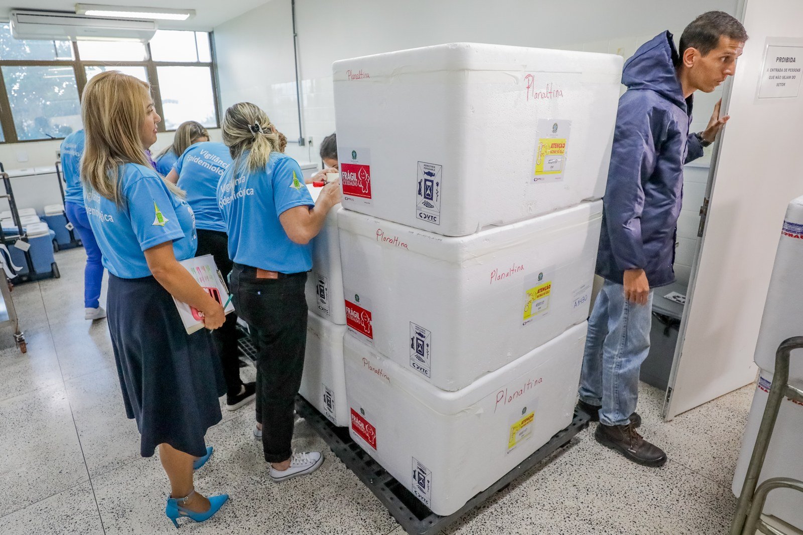 Caixas térmicas empilhadas, etiquetadas com o destino Planaltina, com equipe da vigilância ao lado