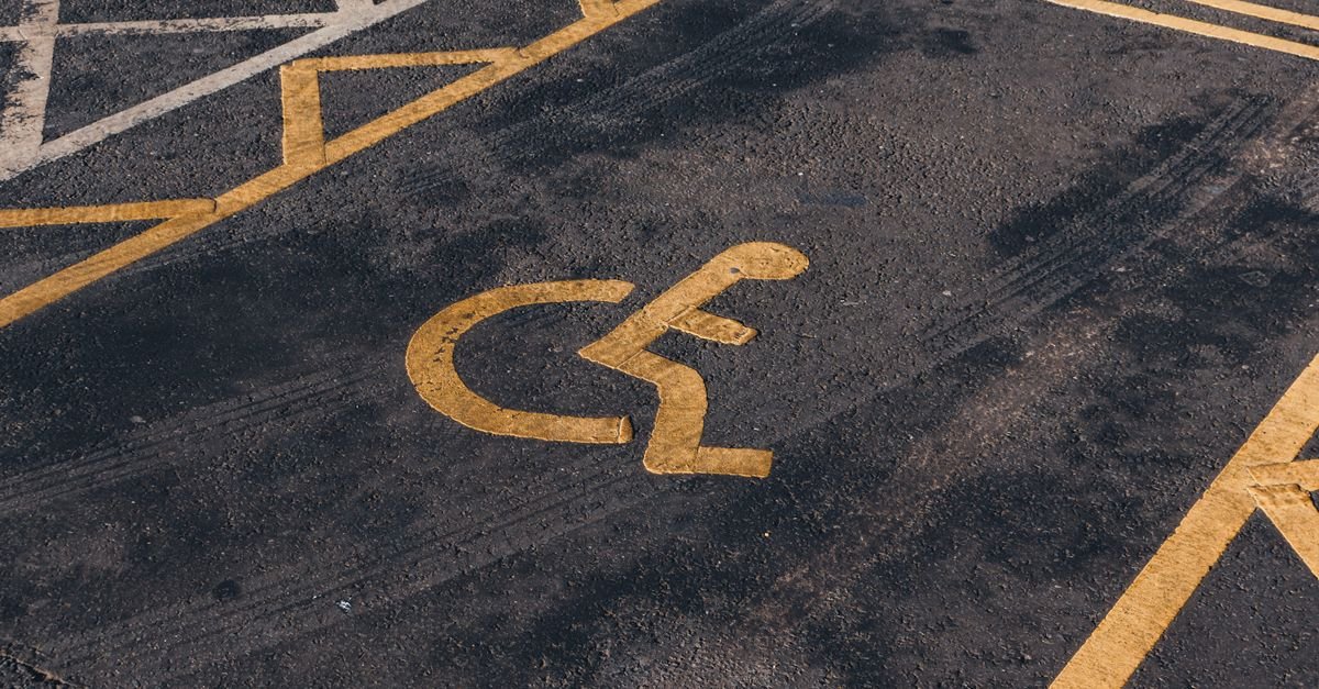 Símbolo internacional de acessibilidade pintado em amarelo no asfalto de uma vaga de estacionamento