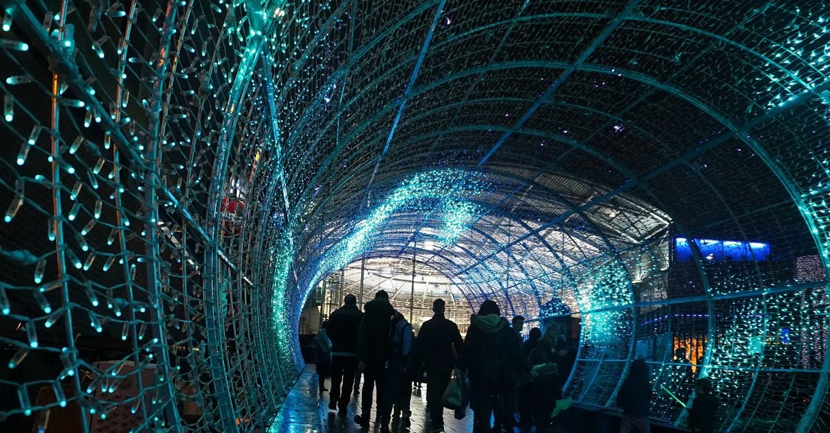 Pessoas caminham dentro de um túnel de luzes de Natal azuis à noite
