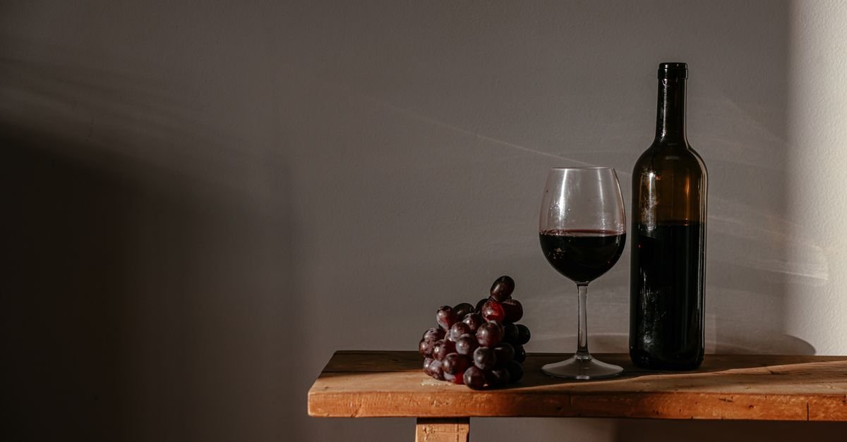 Garrafa de vinho tinto, taça servida e cacho de uvas sobre mesa de madeira