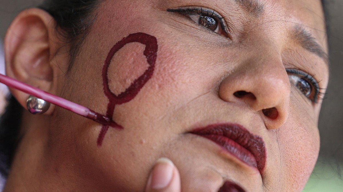 Mulher com o símbolo feminino pintado no rosto, em ato contra a violência de gênero