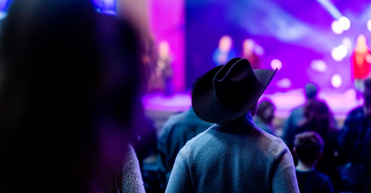 Homem de chapéu de cowboy assiste a show sob luzes roxas e azuis