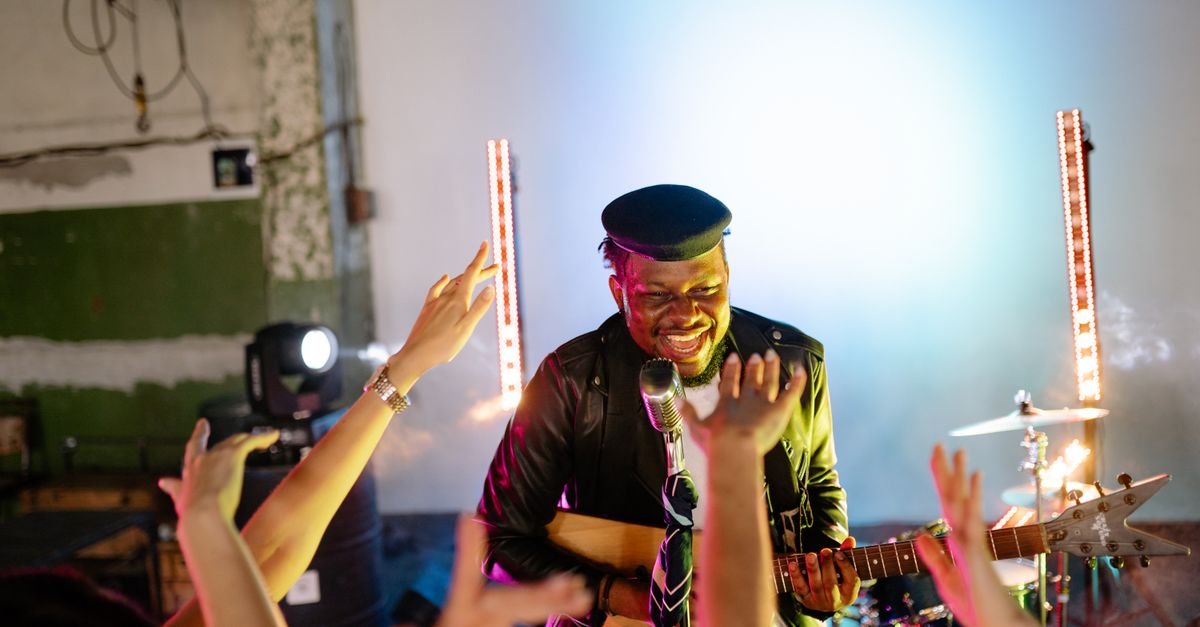 Músico com violão no palco, diante de mãos levantadas do público (foto ilustrativa)