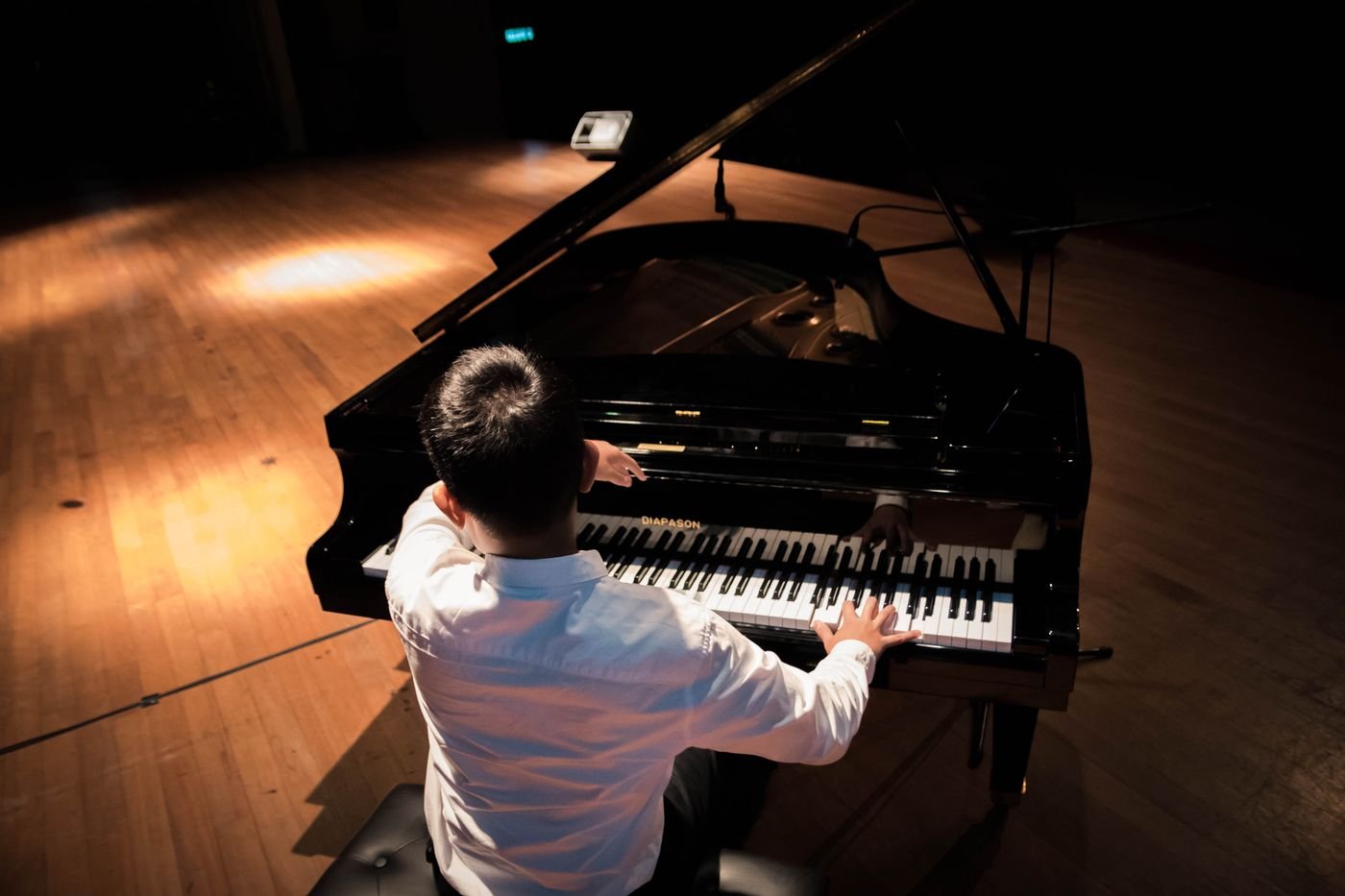 Pianista toca piano de cauda em um palco de madeira visto do alto