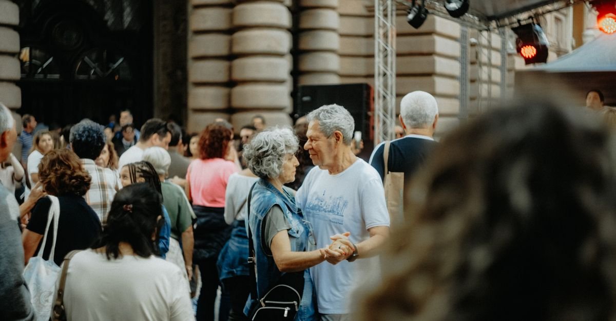 Casal de idosos dança de mãos dadas em meio a uma multidão em festa de rua