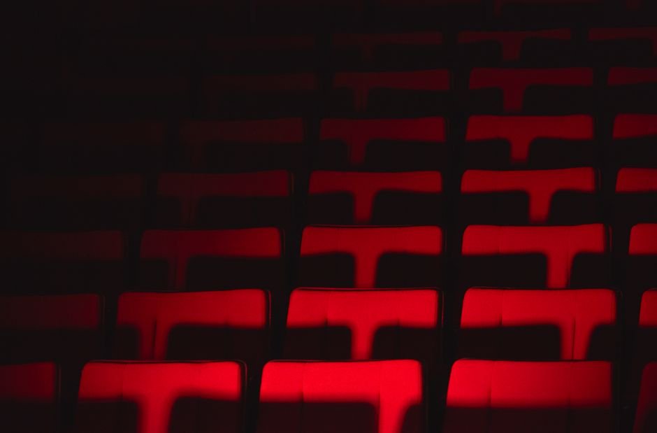 Fileiras de poltronas vermelhas de um teatro iluminadas por um foco de luz