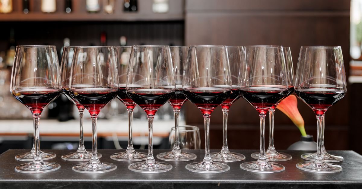 Fileira de taças de vinho tinto servidas sobre o balcão escuro de um bar